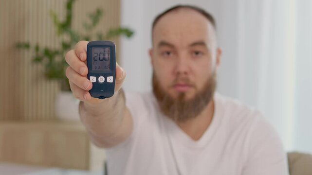 A man holds a glucometer showing a reading of 200 mg dL. He shows concern over the high blood sugar level. This happens in a home environment.