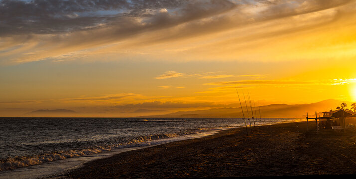 playa con ca&ntilde;as de pescar al atardecer en el mar mediterraneo