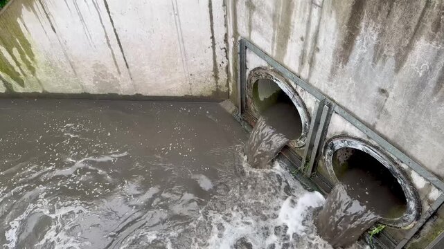 Toxic sewage water pouring from large concrete pipes of a city wastewater treatment facility. Powerful industrial pollution concept with dirty contaminated water