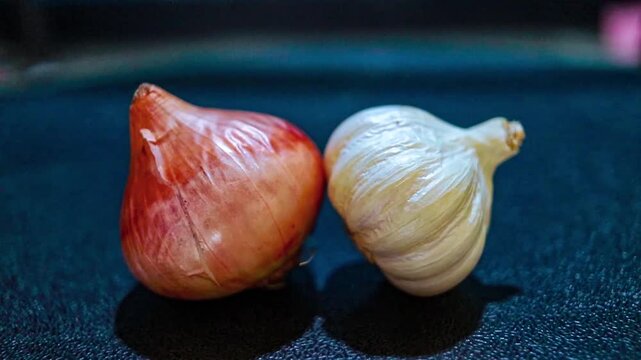 Fresh red onion and white garlic rest side by side on a dark textured surface in this cinematic 4k video clip showing high quality ingredients captured