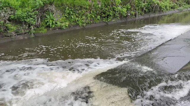 Massive urban wastewater discharge flowing from municipal treatment plant pipes into a polluted water canal.