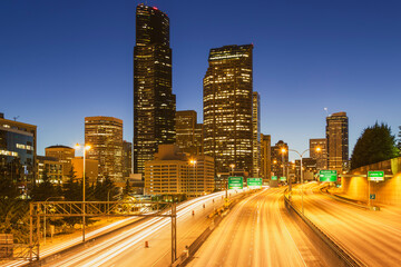 Obraz premium The glowing Seattle skyline is captured at dusk, featuring light trails from traffic on Interstate 5 as it cuts through the heart of downtown.