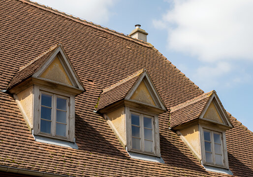 Three brown tiled roof dormer windows against a blue sky background brown tiles house