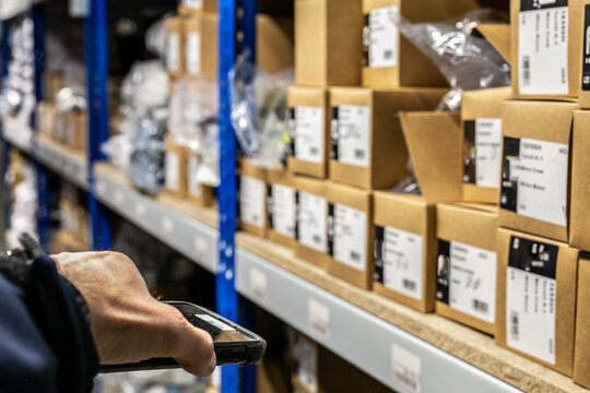 Warehouse worker using a handheld RF scanner (Radio Frequency scanner) to instantly read barcodes on bin locations or items, providing real-time data to Warehouse Management System (WMS) for tracking