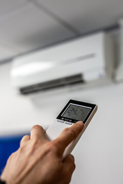 Person using a remote control to operate a wall-mounted white split-system air conditioner inside a modern home. The scene highlights indoor climate control, energy-efficient heating and cooling