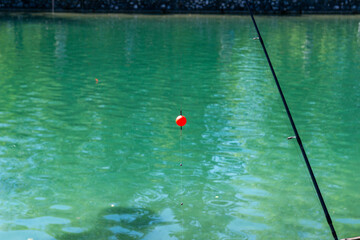 Fishing float over turquoise lake water with fishing rod on a sunny day. © Yulia Antonova