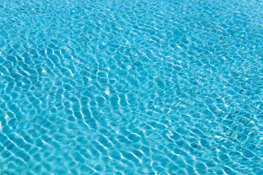 Background Crystal clear turquoise swimming pool water with sunlight ripples and caustics on the bottom.