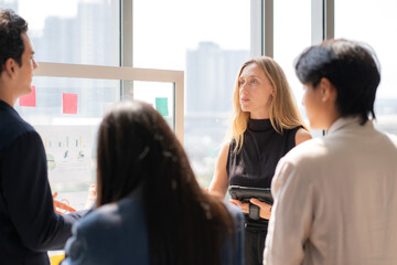 Caucasian businesswoman holding tablet presenting financial report on glass board, colleague team listening during modern office meeting, collaboration and teamwork during project brainstorming. © NT_studio