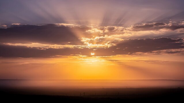 Atmospheric sunset sky with sun rays breaking through layered clouds