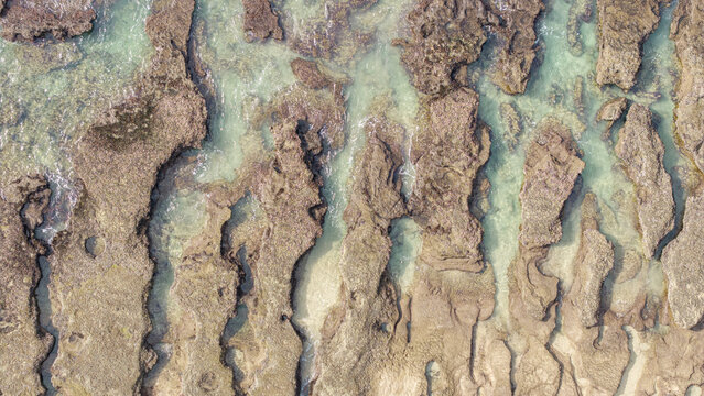 Aerial view of the rugged rock formations and clear turquoise tide pools at Hartenbos in Mossel Bay, Western Cape, South Africa.