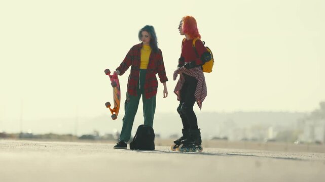 Young female skater and rollerblader friends talking outdoors