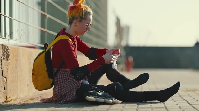 Urban woman with colorful hair bandaging ankle injury after inline skating