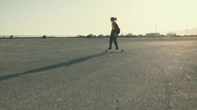 Young woman longboarding in an empty parking lot at sunset