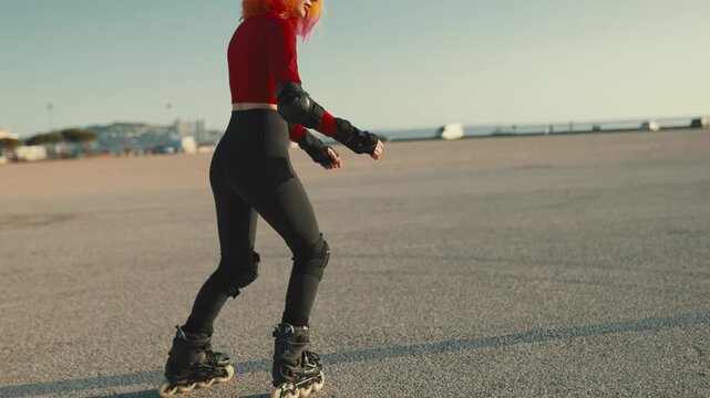 Stylish young woman rollerblading on asphalt at sunset