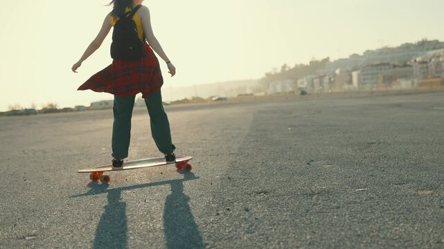 Young woman longboarding on asphalt at sunset