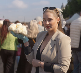Stylish female vendor holding a large lions mane mushroom, Hericium erinaceus in front of a bustling crowd. Naplavka farmers market is a trendy busy weekend hotspot for locals and tourists. © arazu