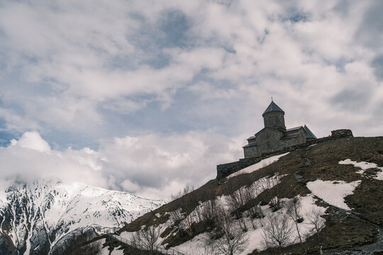 Gergeti Trinity Church standing on a hill under snowy Caucasus peaks in Kazbegi, Georgia. Iconic 14th-century mountain monastery near Stepantsminda under a dramatic cloudy spring sky