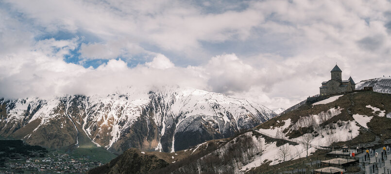 Gergeti Trinity Church standing on a hill under snowy Caucasus peaks in Kazbegi, Georgia. Iconic 14th-century mountain monastery near Stepantsminda under a dramatic cloudy spring sky
