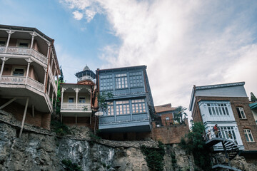 Traditional Georgian houses with colorful carved wooden balconies perched on the Metekhi cliff edge above the Kura river in the old town of Tbilisi, Georgia. Historic architecture at sunset. © Michele