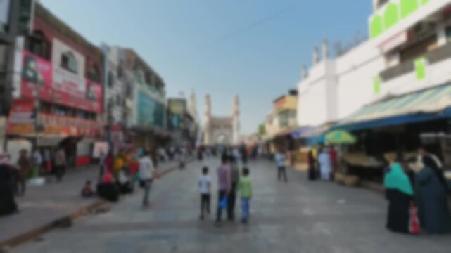 Blurred market street with shops leading toward Charminar landmark at sunrise. Hyderabad urban timelapse concept with soft bokeh crowd motion and historic architecture in old Indian city.