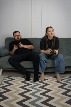 Young couple sitting on a couch, holding game controllers and concentrating intensely while playing video games together in a living room, enjoying leisure time and digital entertainment