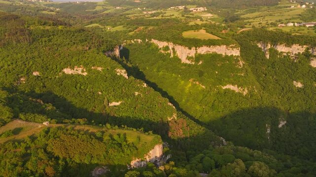 Aerial drone video over lush green Alpine foothills in Italy, with rolling hills, deep gorges and limestone canyon formations in a vibrant natural landscape.