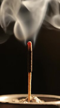 a single lit incense stick. Thin white smoke rises slowly and curls from the glowing tip against a very dark background. Minimal warm lighting. No hands.