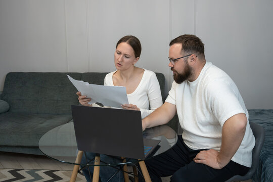 Couple reviewing financial documents, managing personal budget, and using a laptop in their home, indicating financial stress and serious discussions about debt or bills