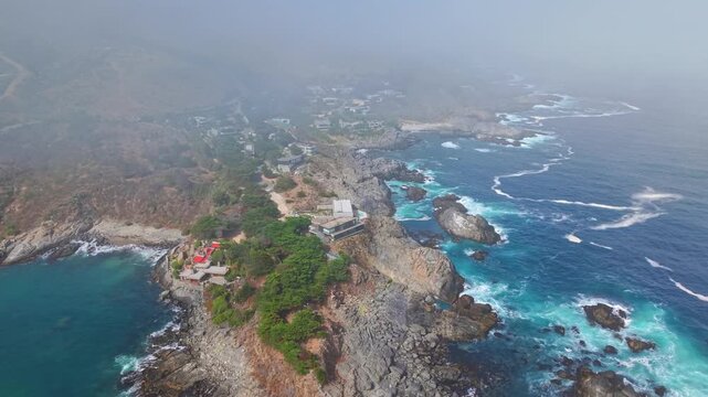 A bird's-eye view orbiting the coast of Pite, with the turquoise waters of the Pacific Ocean visible through low-hanging clouds near Papudo, Chile