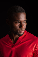 Fototapeta premium Close up of serious African American man looking aside in red shirt on black background