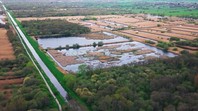 Aerial view of a wetland nature reserve with ponds, reed beds, and surrounding farmland divided by drainage channels and a canal. Rural landscape showing natural habitat and land use.