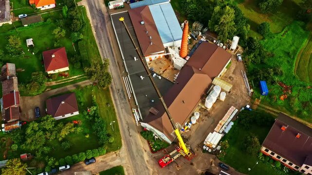 Dairy plant with crane operating by industrial buildings, surrounding homes, aerial top view
