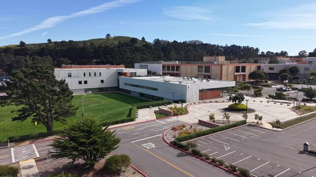 Sunny afternoon aerial perspective of the modern architecture and empty parking lot of Skyline College in San Bruno, California, with lush green hills visible in the background