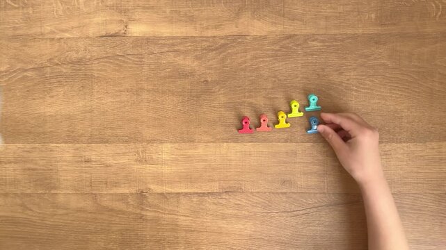 child hands placing six small colorful clips in a row on wooden table slow motion 4K