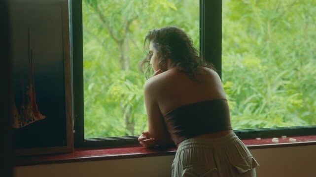Woman leans on window ledge and looks outside in peaceful indoor setting