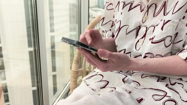 Hand uses smartphone by a bright window. Close up mobile tapping beside city glass in an indoor setting. App browsing and urban lifestyle content..
