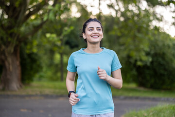 Fototapeta premium Young indian woman feeling positive and healthy while running outdoors, wearing sportswear and a smartwatch, focusing on her fitness goals in a green park environment
