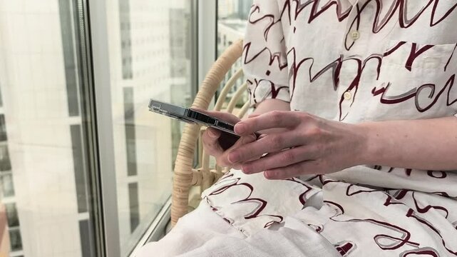 Hands use a smartphone beside a bright city window. Fingers tap and adjust the device in close up indoor view. Mobile browsing and urban lifestyle concept..