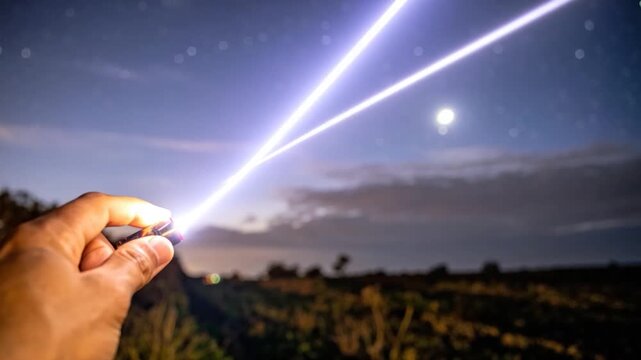Hand holding flashlight at night with bright light beams illuminating the starry sky