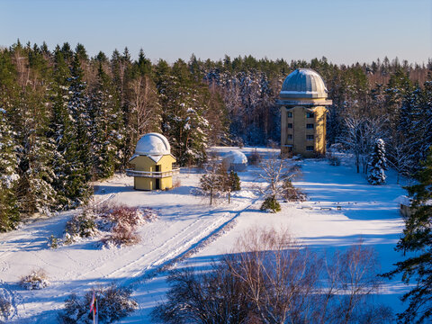 Aerial view of the Moletai Astronomical Observatory with its distinctive domes nestled in a snow-covered pine forest under bright winter sunlight Kulionys, Utenos apskritis, Lithuania.