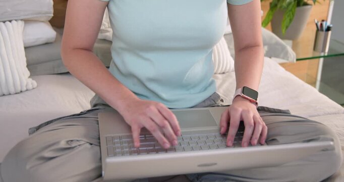 Female typing on laptop while working on bed with smartwatch, camera pulling back, smiling