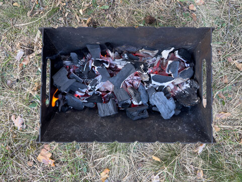 Smoldering coals in a portable metal grill, close-up of an outdoor barbecue with hot coals for shashlik