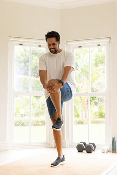 African American man wearing white tee, blue shorts stretching on woven mat at home near weights