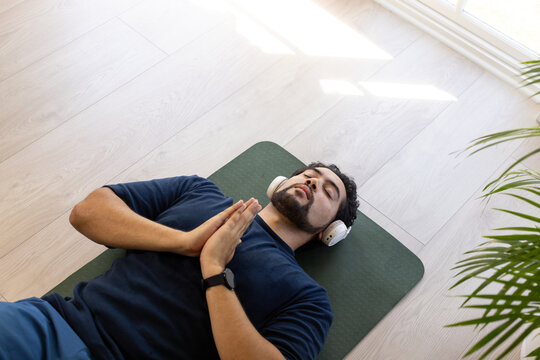 Mid adult African American man lying on green mat at home, wearing navy shirt headphones smartwatch