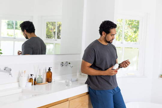 African American man standing at home vanity rubbing product from white bottle, copy space
