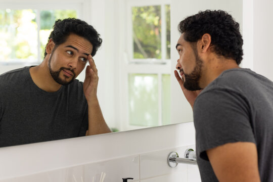 Middle-aged African American man examining face in mirror at bathroom sink, touching temple