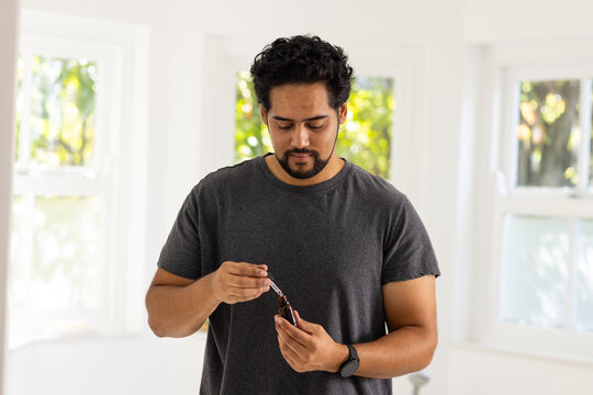 African American man examining dropper bottle and using pipette at home wearing wristwatch
