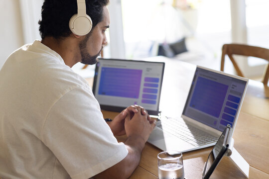 Mid adult African American man sitting at wooden table using two laptops and tablet, copy space