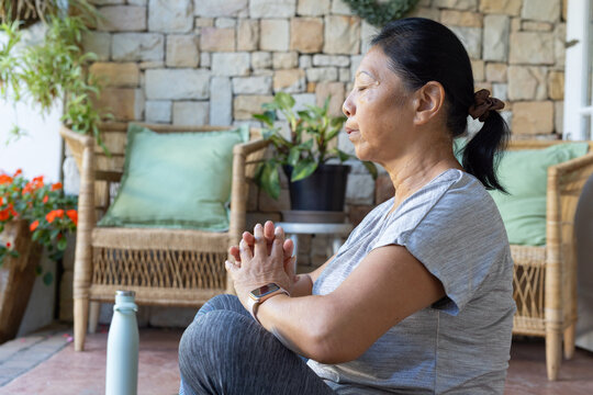 Senior Asian woman sitting right porch clasping wearing smartwatch bottle wicker-chair, copy space