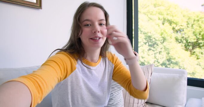 Woman sitting on couch by window reaching, adjusting phone, smiling, waving, connecting with viewer